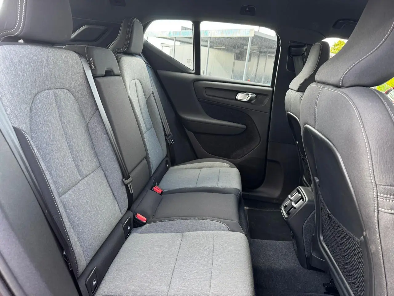 Vue latérale des sièges arrière gris clair et noir du Volvo XC40 2024, avec aérateurs et port USB au centre.