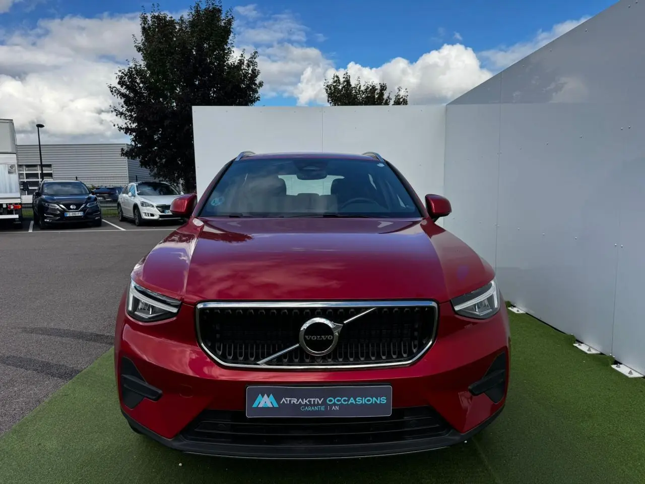 Vue frontale d'un Volvo XC40 Fusion Red Metal 2024 avec calandre noire et détails chromés, sur fond extérieur urbain.