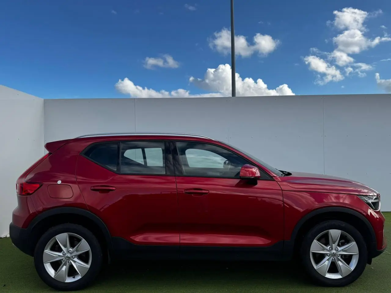 Profil côté gauche du Volvo XC40 2024 en rouge Fusion Metal avec jantes alliage 18 pouces sur fond clair.
