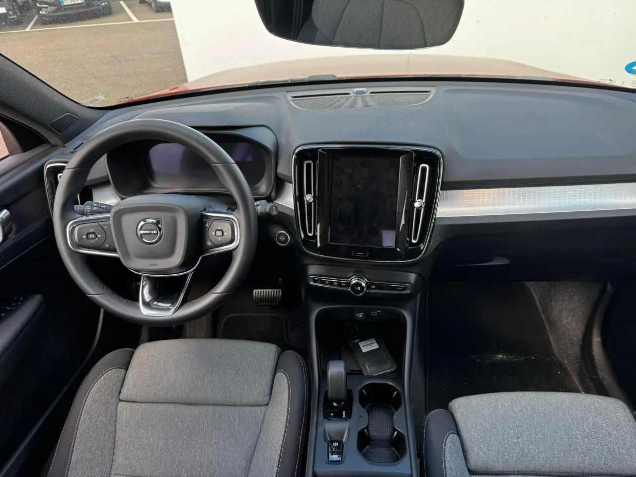 Vue intérieure frontale du tableau de bord et volant cuir du Volvo XC40 2024 avec écran tactile central et sièges gris.