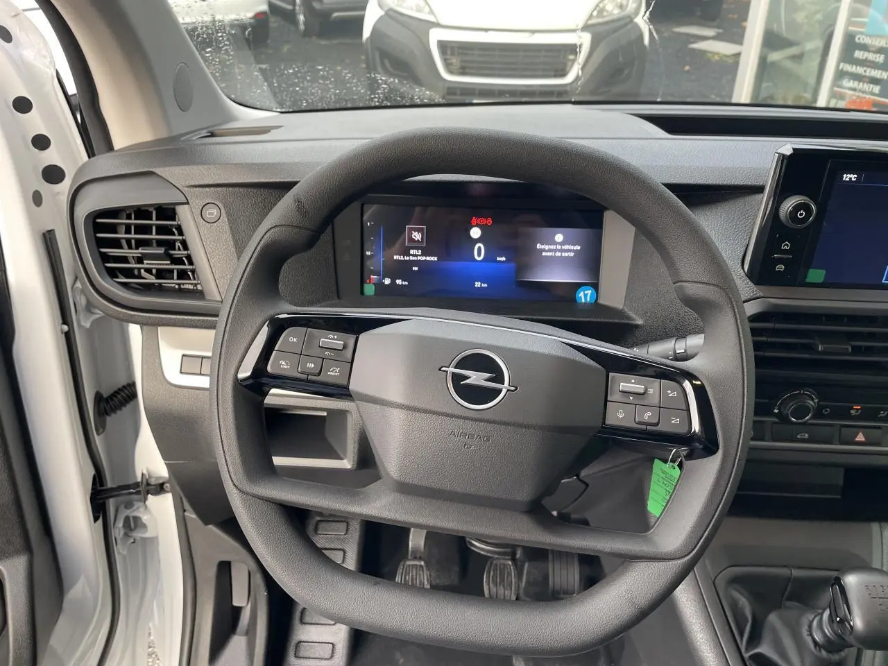 Vue intérieure centrée sur le volant noir d’un Opel Vivaro blanc 2024 avec combiné numérique et levier de vitesse manuel.