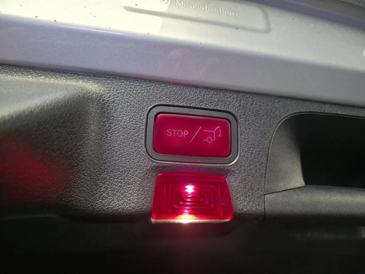 Gros plan sur le bouton rouge d'ouverture/fermeture automatique du hayon dans le coffre d'une Mercedes CLA Shooting Brake gris.
