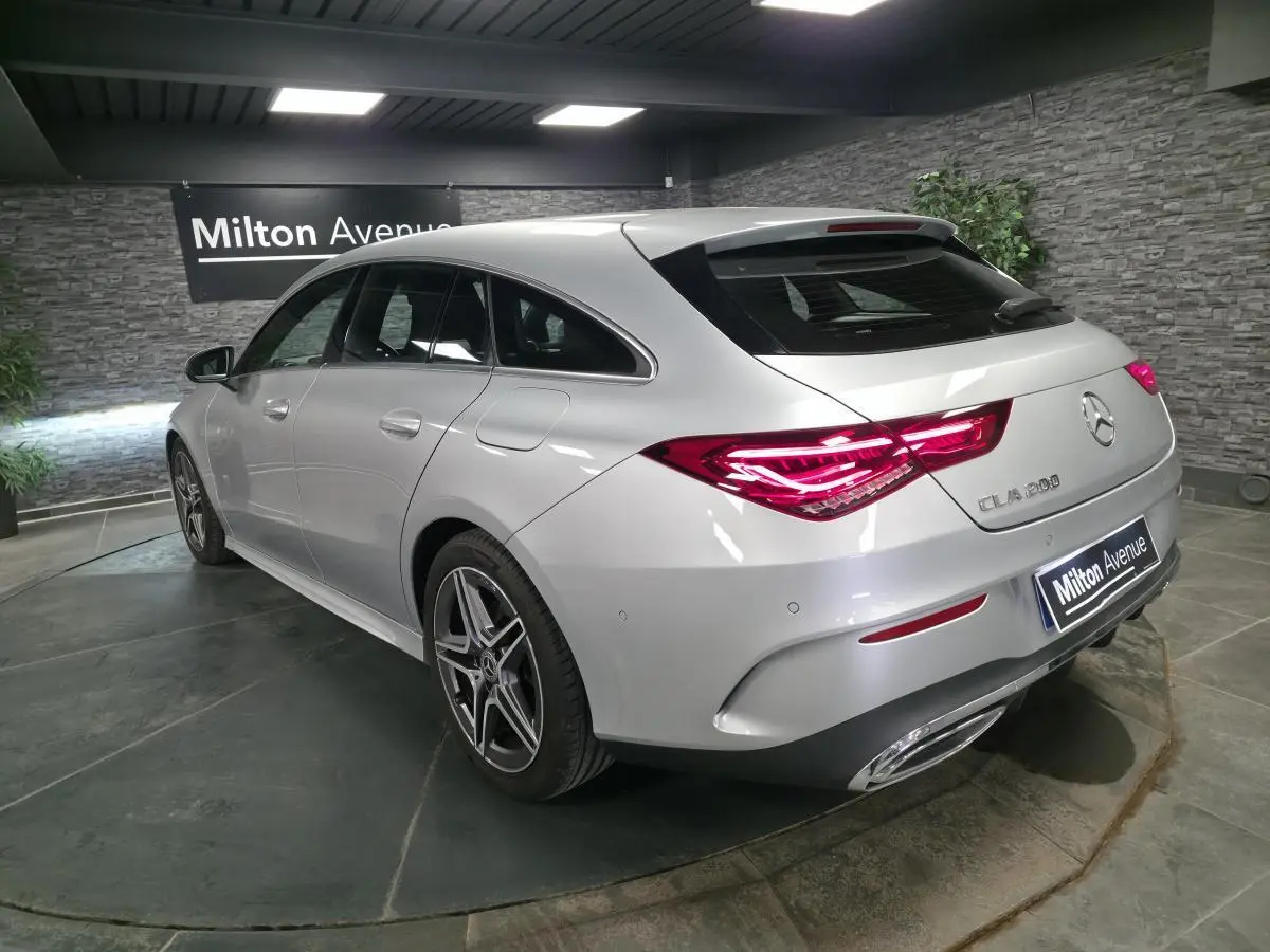Vue 3/4 arrière droite d'une Mercedes CLA Shooting Brake 200 gris métallisé avec jantes AMG et feux arrière LED allumés.