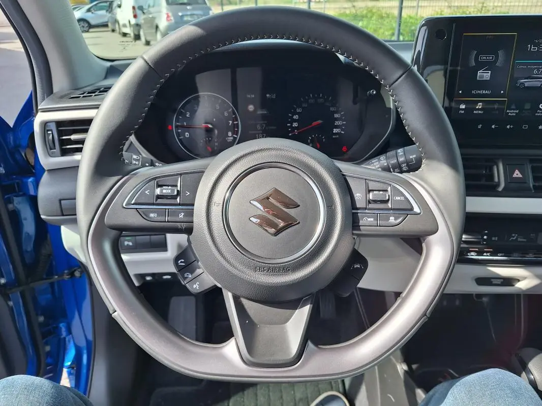 Vue centrée sur le volant noir de la Suzuki Swift bleu 2025, avec tableau de bord et écran tactile visibles.