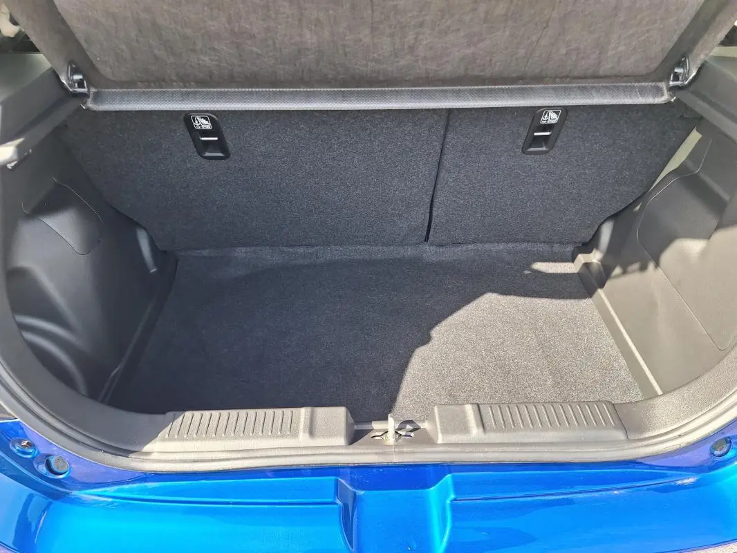 Coffre ouvert vu de l'arrière d'une Suzuki Swift 2025 bleu, montrant l'espace de chargement vide et la garniture intérieure.