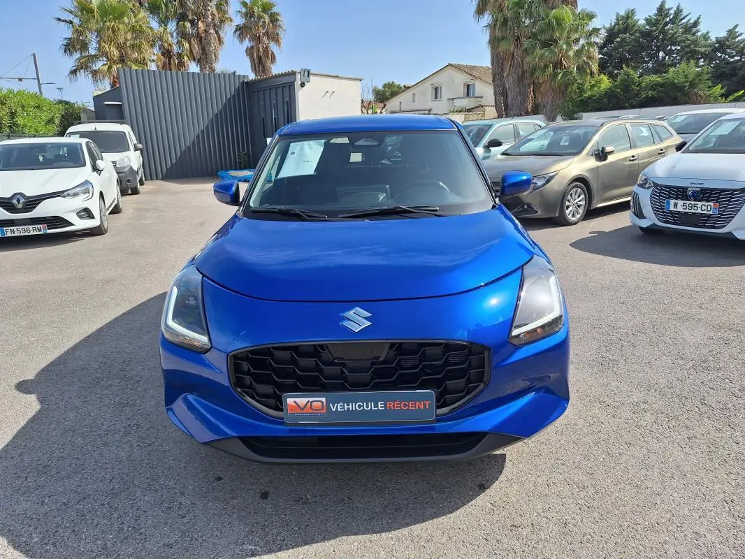 Vue avant d'une Suzuki Swift 1.2 Dualjet Hybrid Privilege bleu vif avec calandre noire et feux LED allumés.