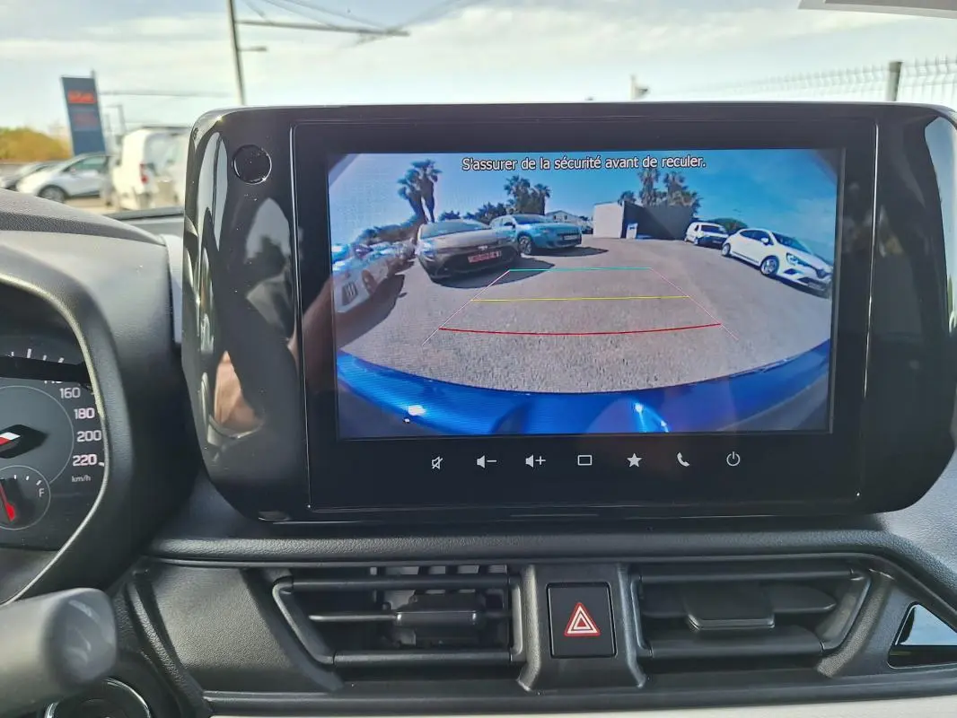 Vue intérieure du tableau de bord d'une Suzuki Swift 2025 avec écran tactile affichant la caméra de recul et le capot bleu visible.