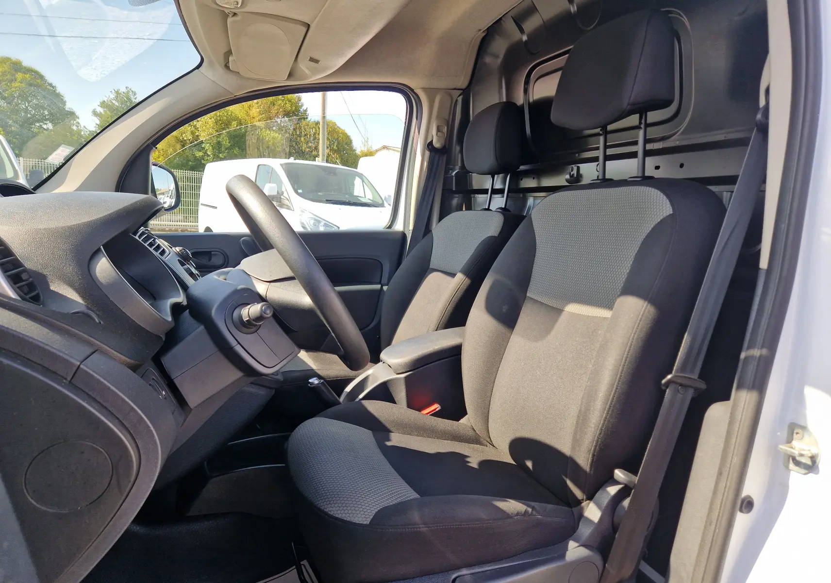 Intérieur du Renault Kangoo blanc 2021 vu côté conducteur, montrant les sièges avant et le tableau de bord simple.