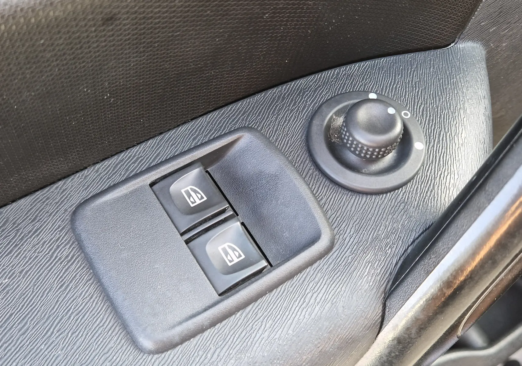 Gros plan sur les commandes électriques des vitres et le réglage des rétroviseurs côté conducteur d’un Renault Kangoo blanc.