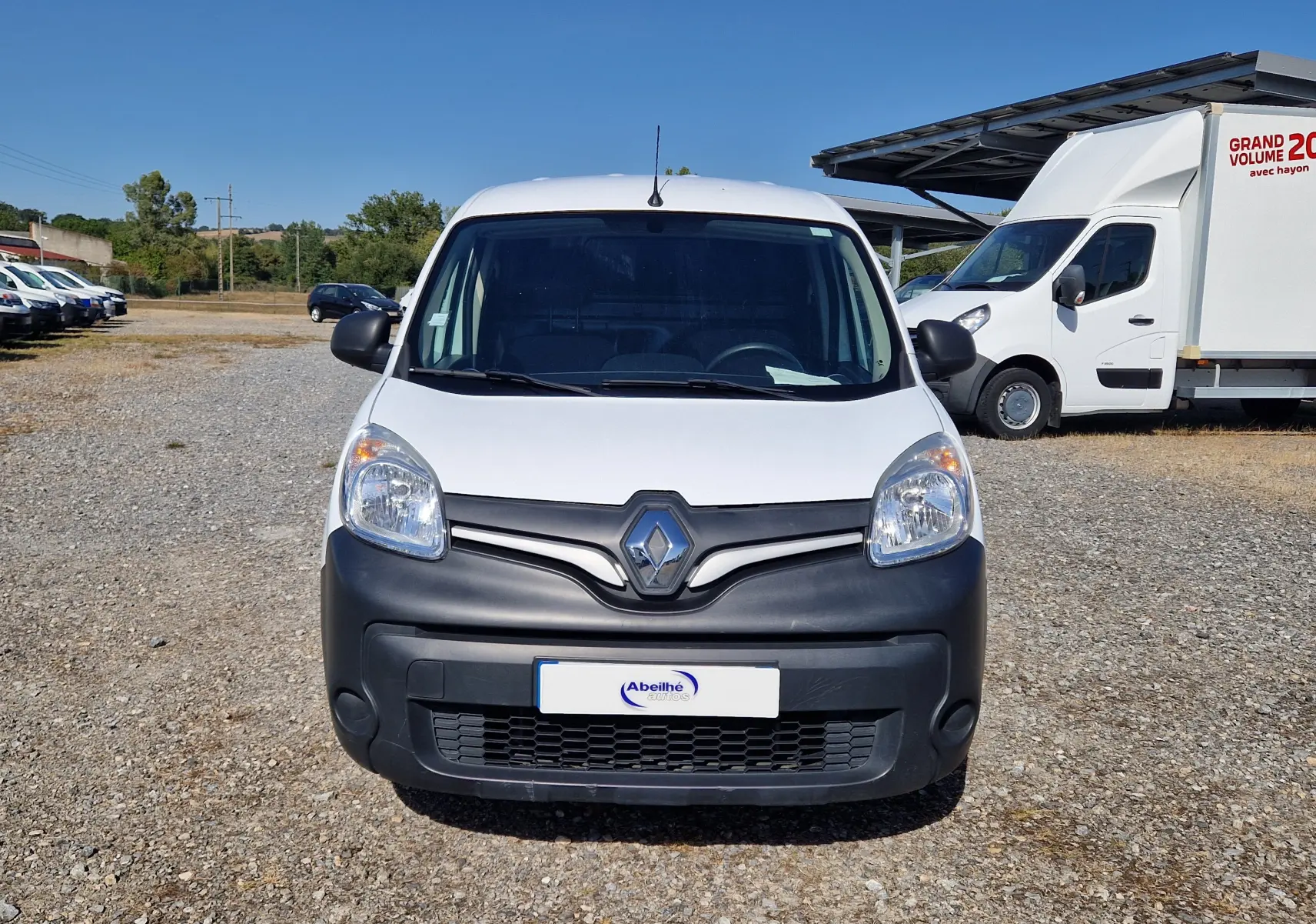 Vue avant d'un Renault Kangoo blanc 2021 avec pare-chocs noir mat sur un terrain gravillonné en extérieur.