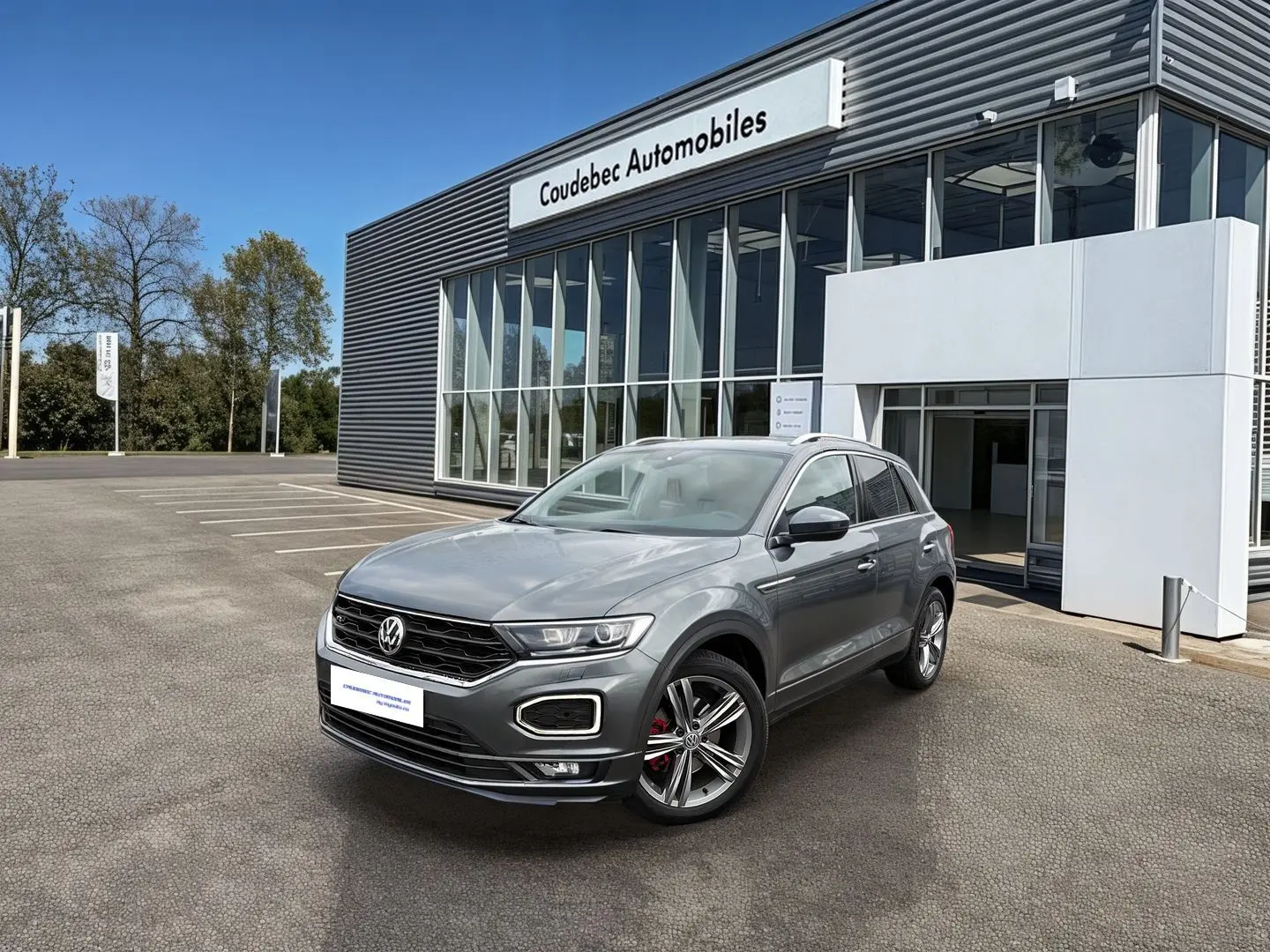 Volkswagen T-Roc gris Indium métal en 3/4 avant droit, avec jantes alliage et calandre R-Line visible.