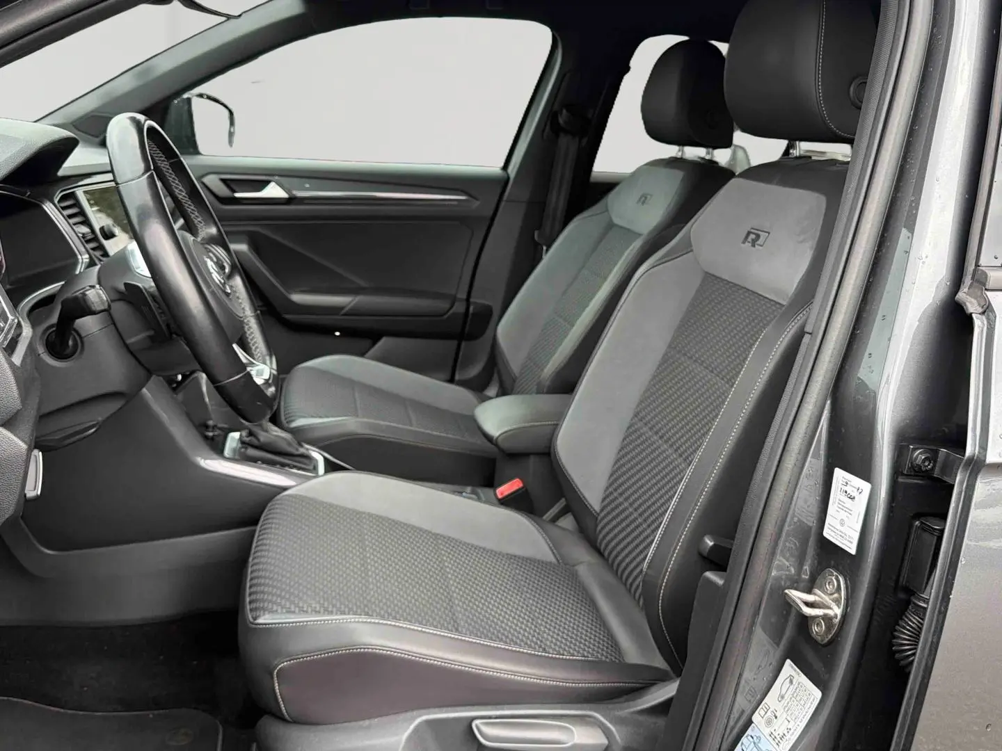 Vue intérieure côté conducteur du Volkswagen T-Roc gris Indium, sièges R-Line en similicuir avec surpiqûres grises.