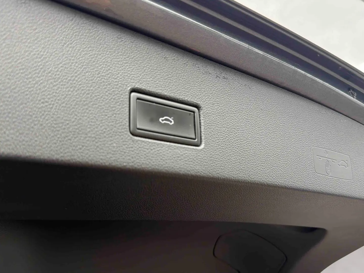 Gros plan sur le bouton d'ouverture électrique du coffre du Volkswagen T-Roc gris Indium, intérieur du hayon visible.