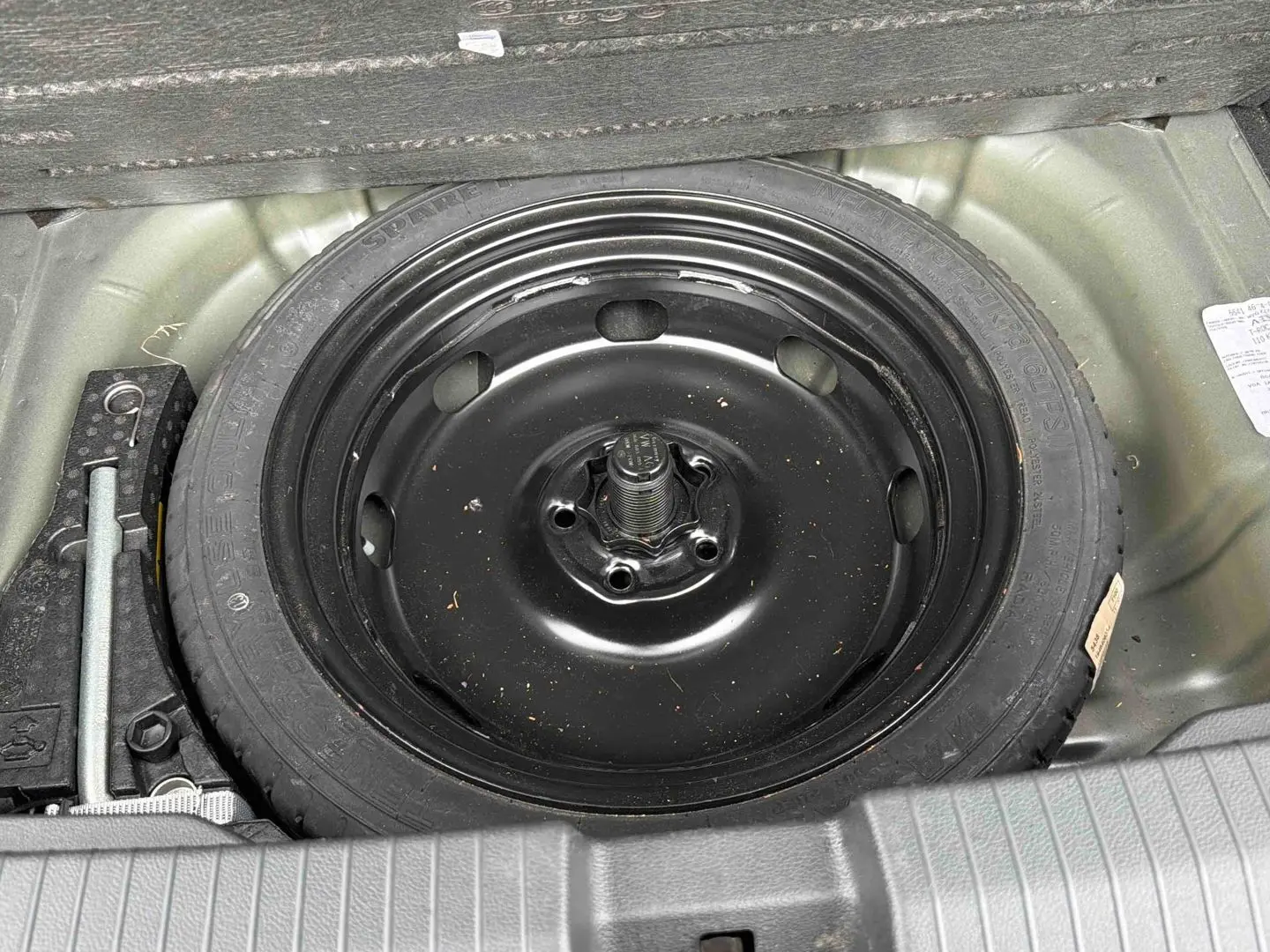 Vue plongeante sur la roue de secours noire et les outils dans le coffre du Volkswagen T-Roc gris Indium Metal.