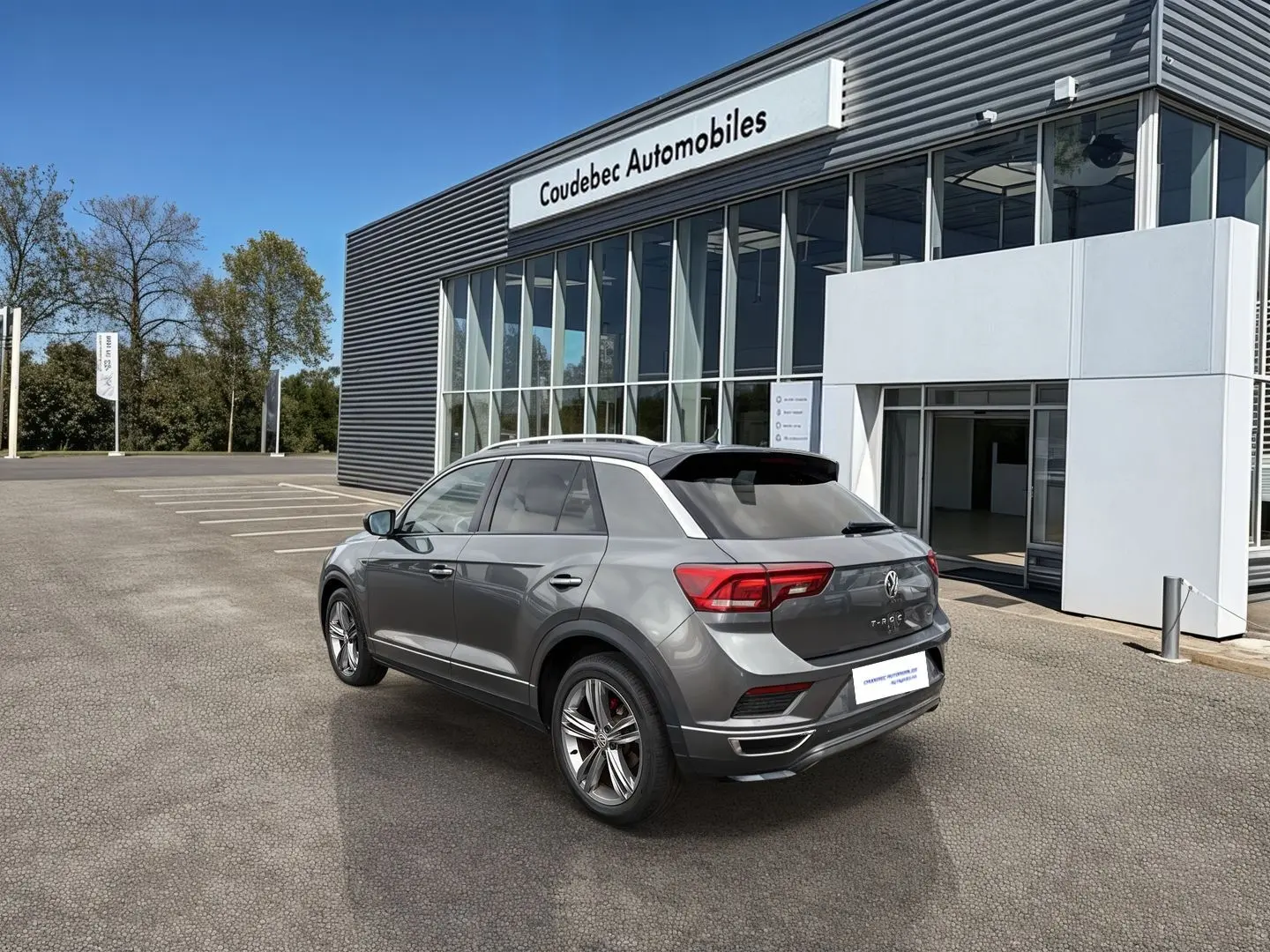 Volkswagen T-Roc gris Indium métal en 3/4 arrière droit, avec jantes alliage et feux LED, devant concession.