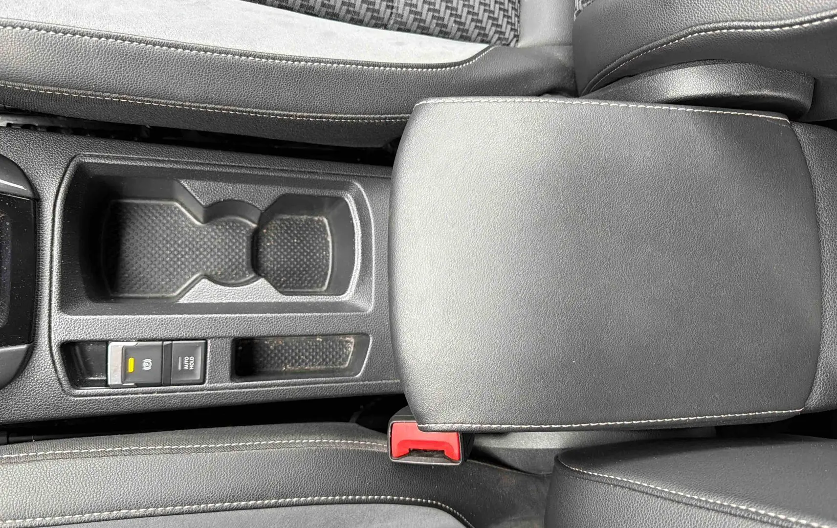 Vue plongeante sur l'accoudoir central en similicuir noir et la console centrale du Volkswagen T-Roc gris Indium.