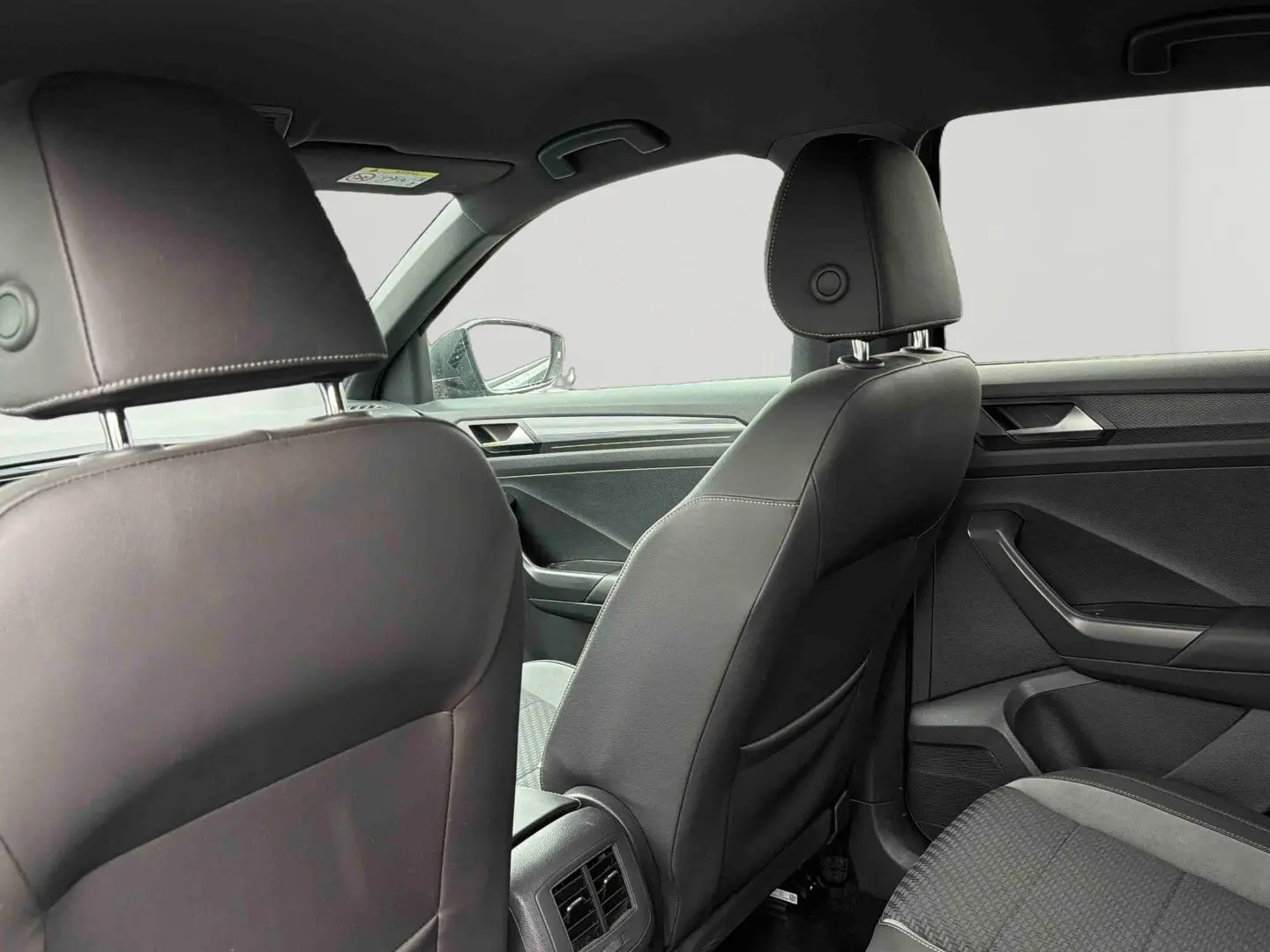Vue intérieure arrière du Volkswagen T-Roc 2020 avec sièges en similicuir noir et détails modernes sur les portières.