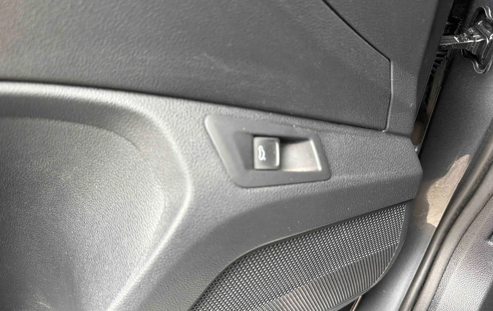 Détail du panneau intérieur de porte avec bouton d'ouverture du coffre sur Volkswagen T-Roc gris Indium.