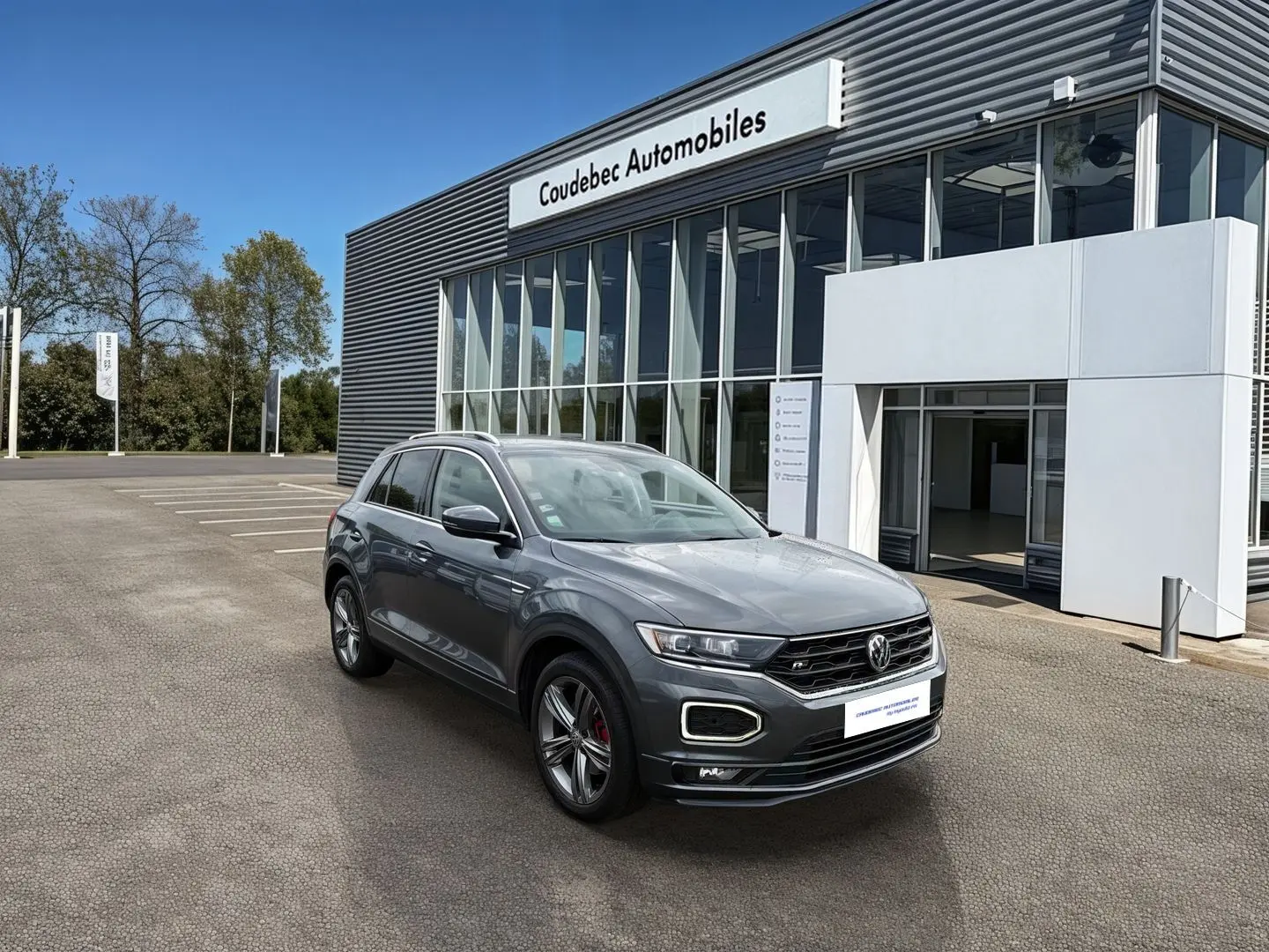 Volkswagen T-Roc gris Indium métal en 3/4 avant droit, avec jantes alliage 18 pouces et détails R-Line visibles.