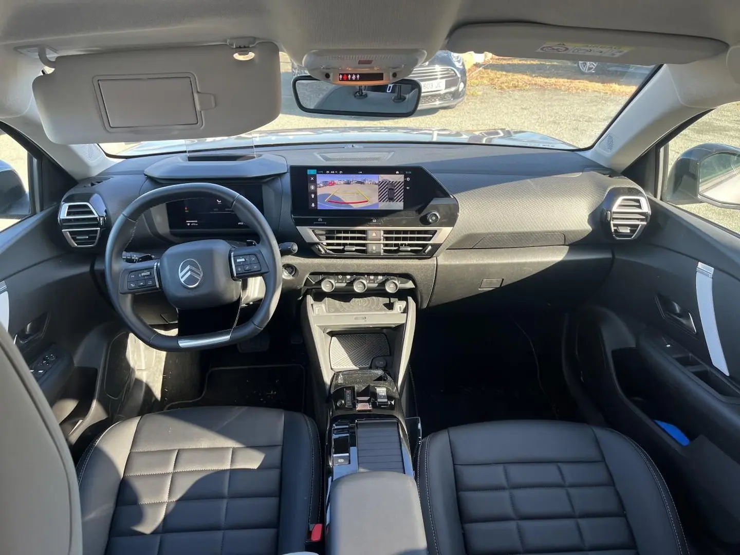 Intérieur Citroën C4 X hybride 2025 vu de face, tableau de bord moderne avec écran tactile et sièges cuir noirs.