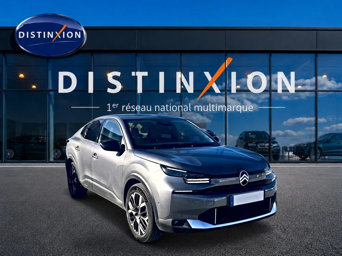 Citroën C4 X gris mercure vue 3/4 avant droit, avec calandre distinctive et jantes alu devant un showroom Distinxion.