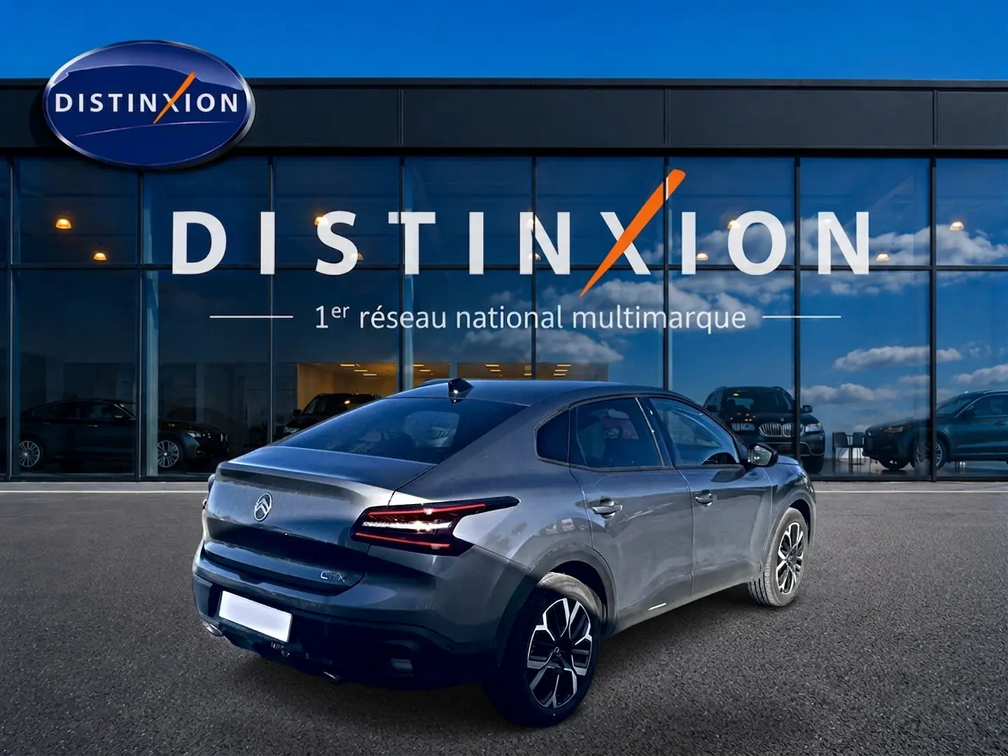 Vue 3/4 arrière droite d'une Citroën C4 X gris mercure avec feux arrière LED et jantes alu devant un showroom Distinxion.