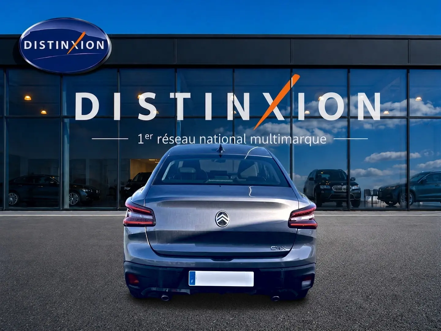 Vue arrière d'une Citroën C4 X gris mercure garée devant une vitrine avec logo Distinxion.