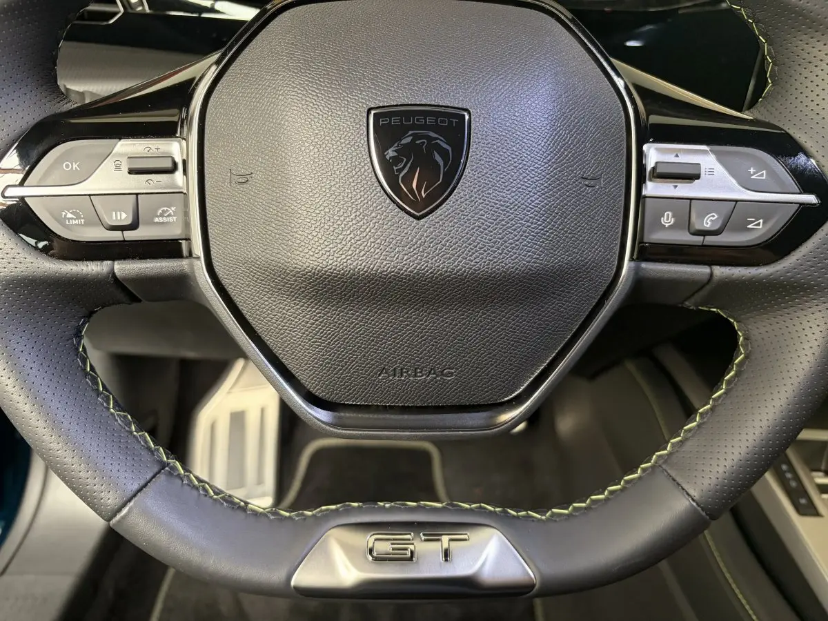 Gros plan sur le volant cuir perforé noir avec logo Peugeot et badge GT, intérieur Peugeot 308 hybride 2025.