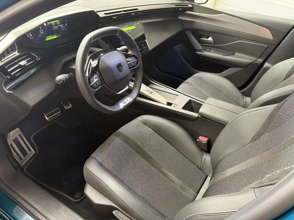 Vue intérieure côté conducteur de la Peugeot 308 GT 2025, avec volant cuir multifonctions et sièges tissu/cuir gris.
