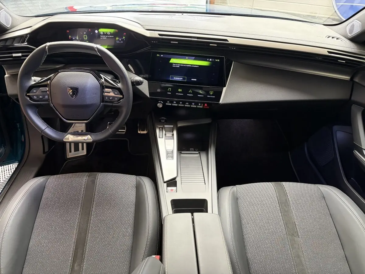 Intérieur de la Peugeot 308 hybride 2025, vue de dessus sur le tableau de bord et volant cuir noir avec écran tactile central.