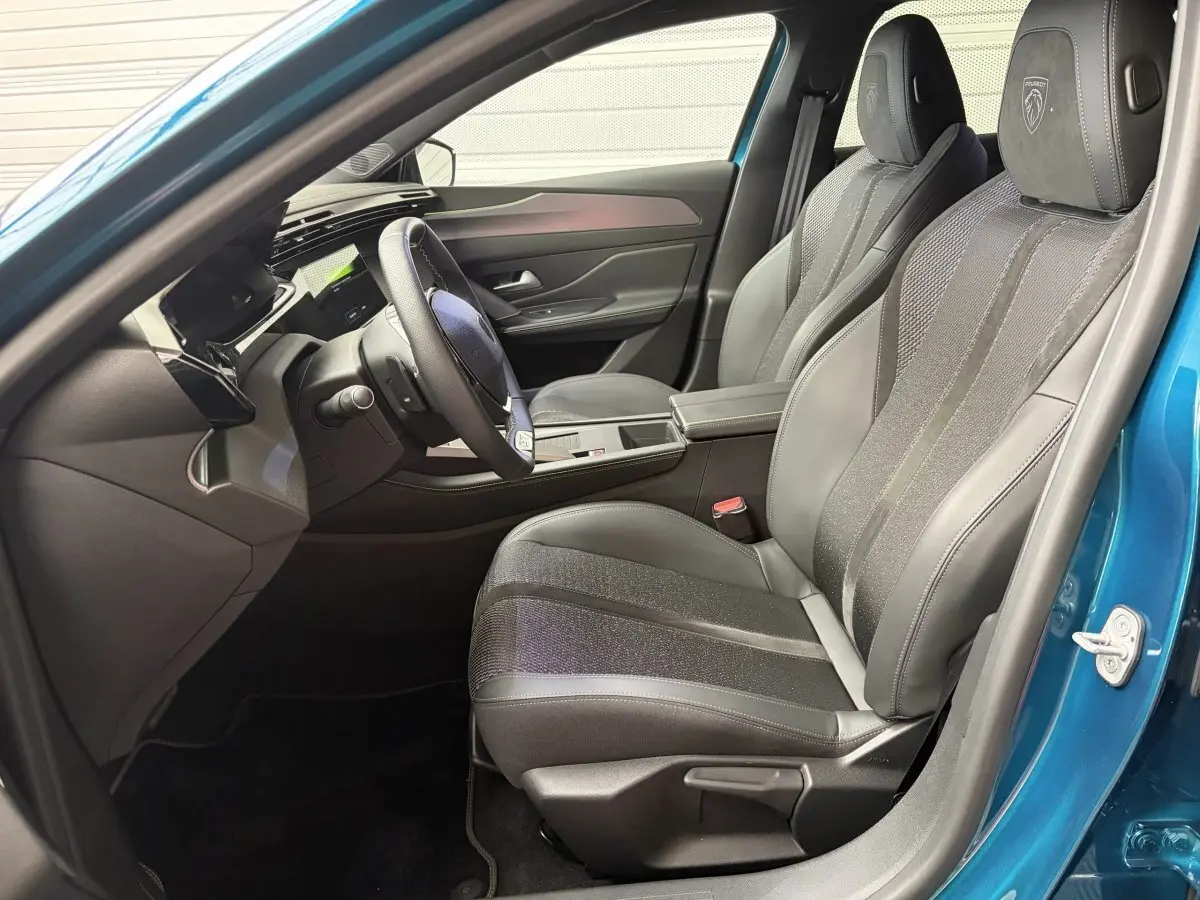 Intérieur avant droit de la Peugeot 308 bleu 2025, sièges cuir noirs avec logo Peugeot brodé sur appuie-tête.
