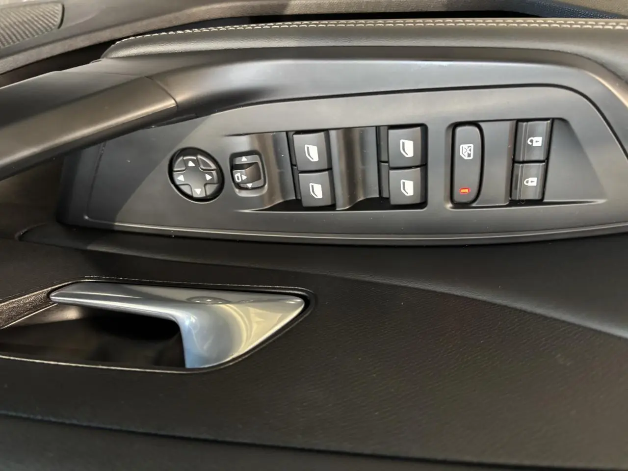 Vue rapprochée des commandes de lève-vitres et rétroviseurs côté conducteur sur porte intérieure noire d’une Peugeot 308 SW gris clair.