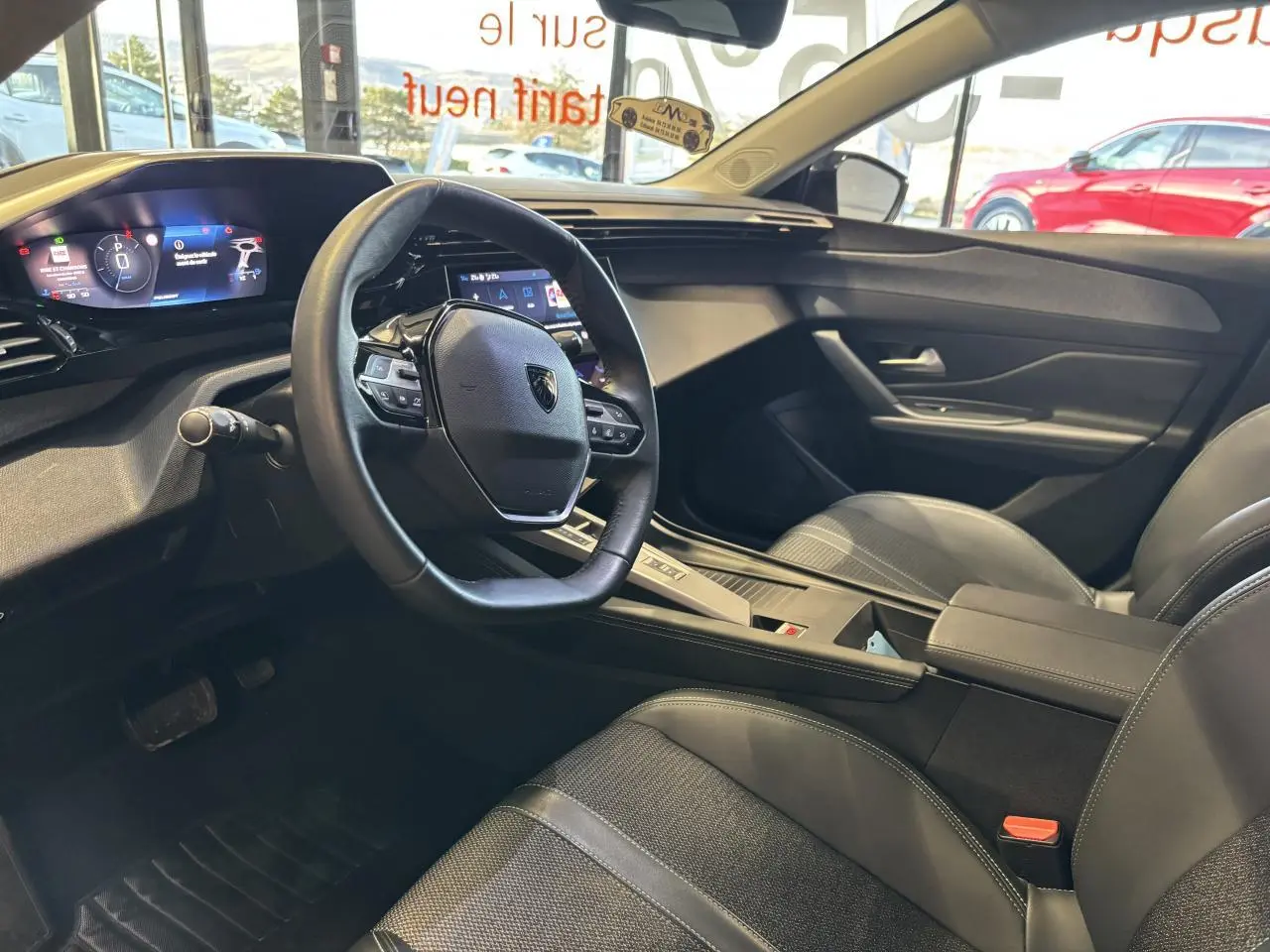 Vue intérieure côté conducteur de la Peugeot 308 SW 2024 avec volant cuir, tableau de bord numérique et sellerie tri matières noire.