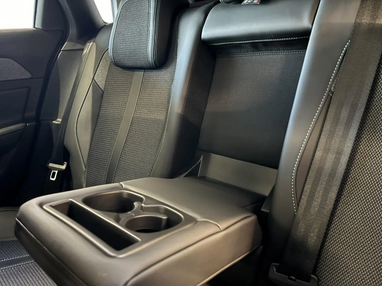 Détail de l'accoudoir central arrière avec porte-gobelets sur la banquette tissu noir de la Peugeot 308 SW 2024.