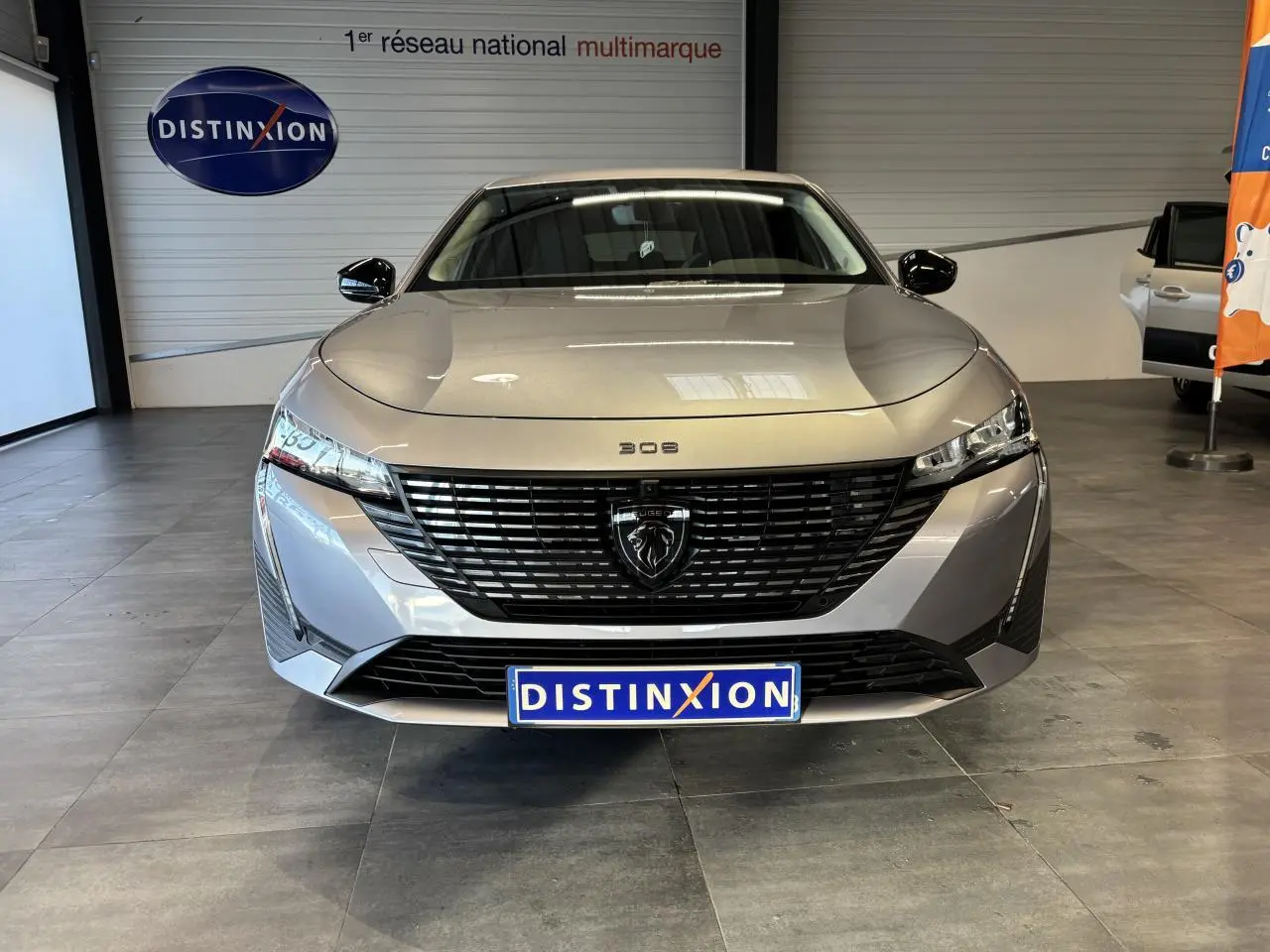Vue frontale d'une Peugeot 308 SW gris clair métallisé avec calandre noire et logo lion central, en showroom.