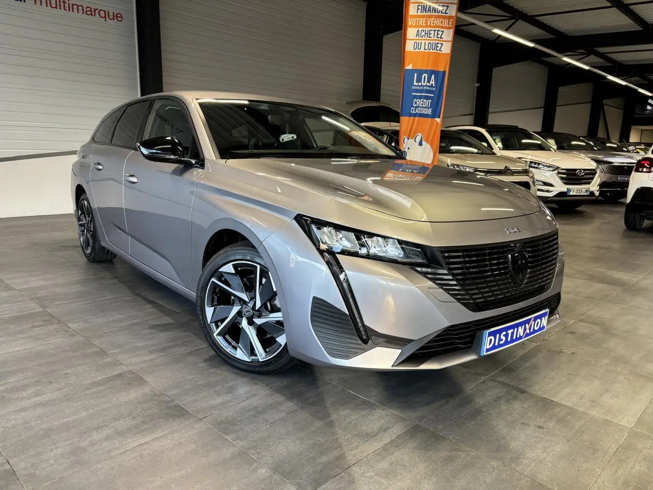 Peugeot 308 SW gris clair métallisé vue 3/4 avant droit en intérieur avec jantes alliage et calandre noire.