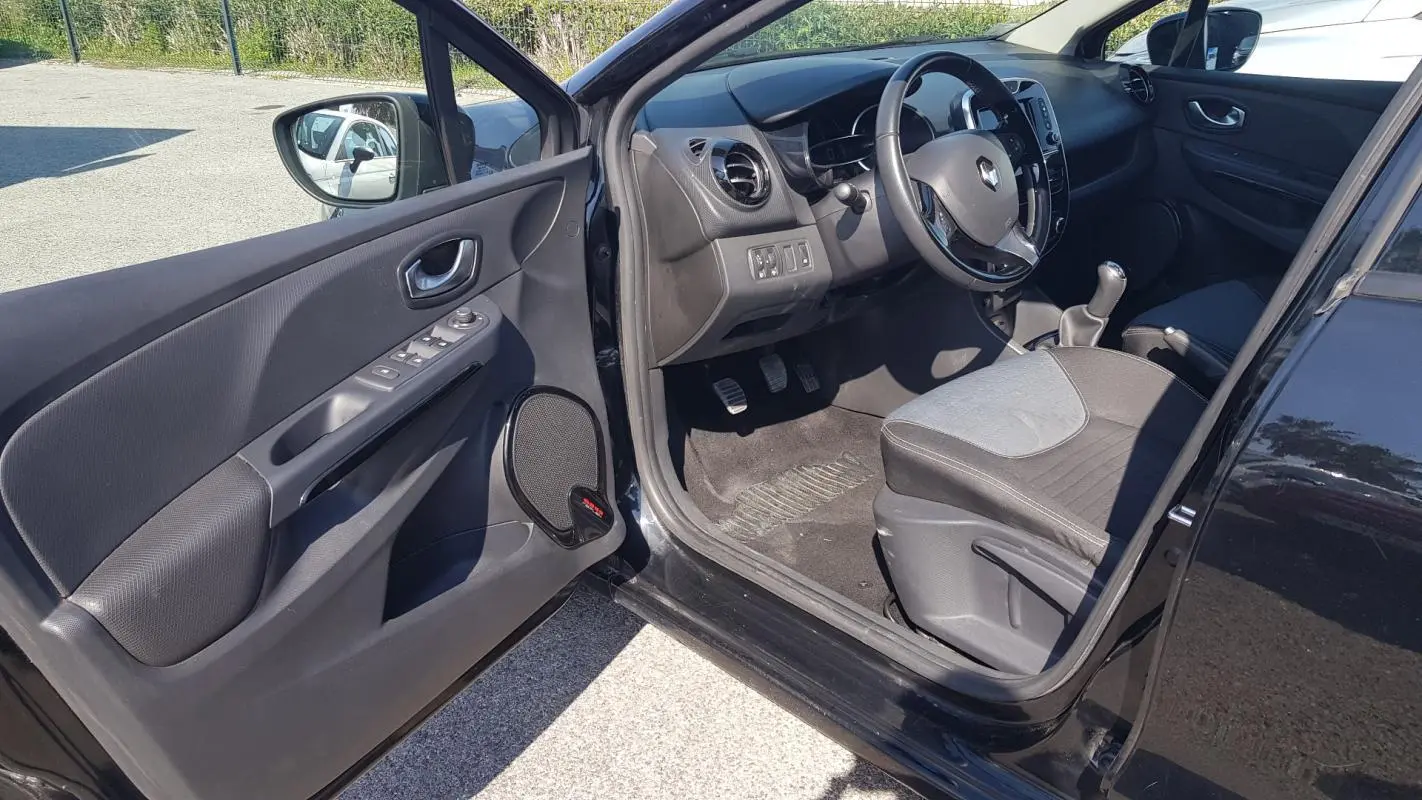 Vue intérieure côté conducteur d'une Renault Clio IV noire, montrant le volant cuir, la boîte manuelle et les commandes de porte.