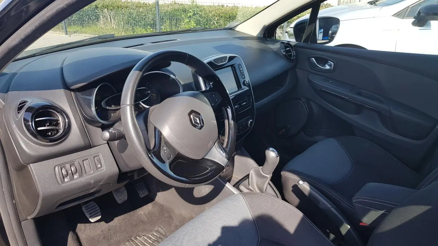 Vue intérieure côté conducteur de la Renault Clio IV noire, montrant le volant cuir, tableau de bord et levier de vitesse manuel.