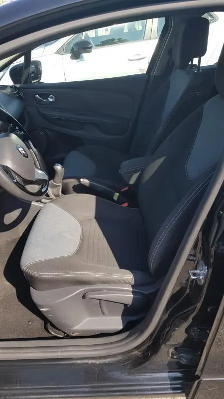 Vue intérieure côté conducteur de la Renault Clio IV noire, siège tissu avec réglage hauteur et volant cuir visible.