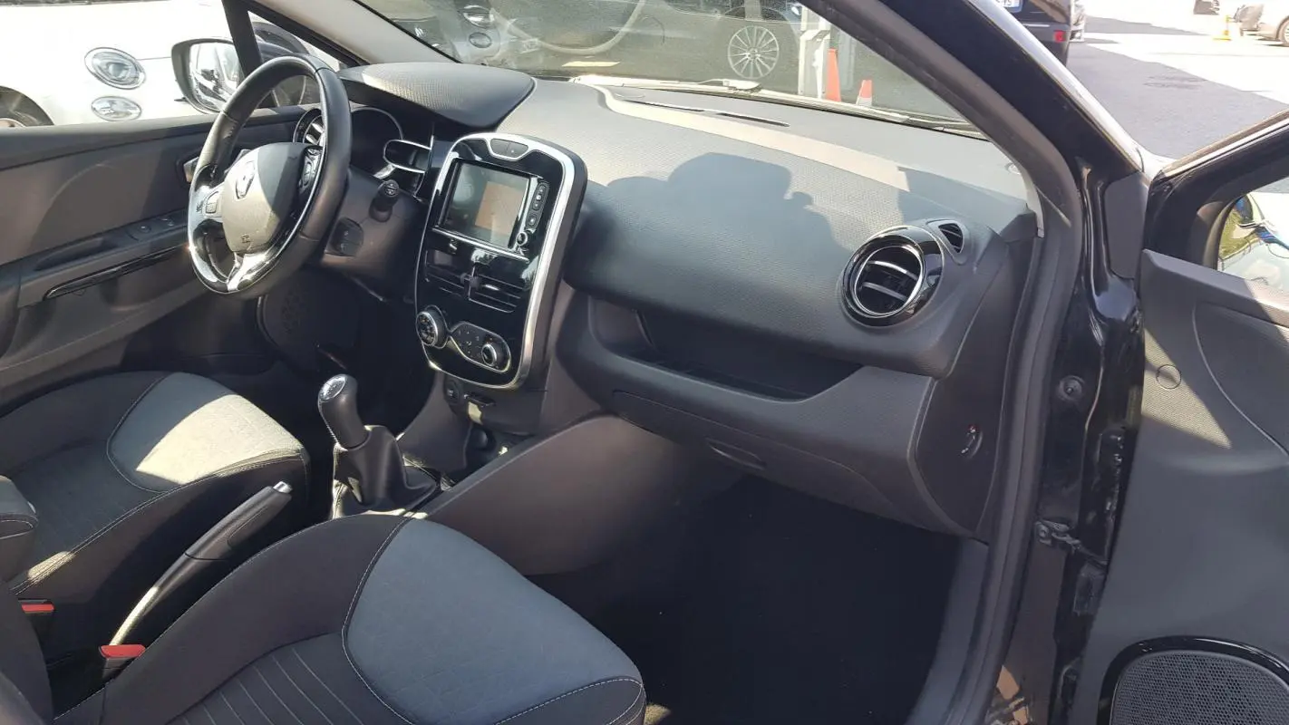 Vue intérieure côté passager de la Renault Clio IV noire, montrant tableau de bord et console centrale avec écran tactile.