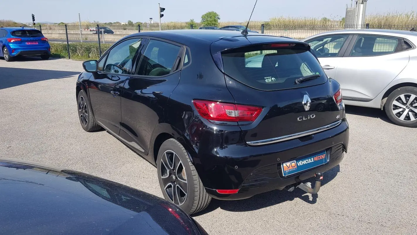 Vue 3/4 arrière droite d'une Renault Clio IV noire avec jantes alliage 16 pouces et attelage visible.