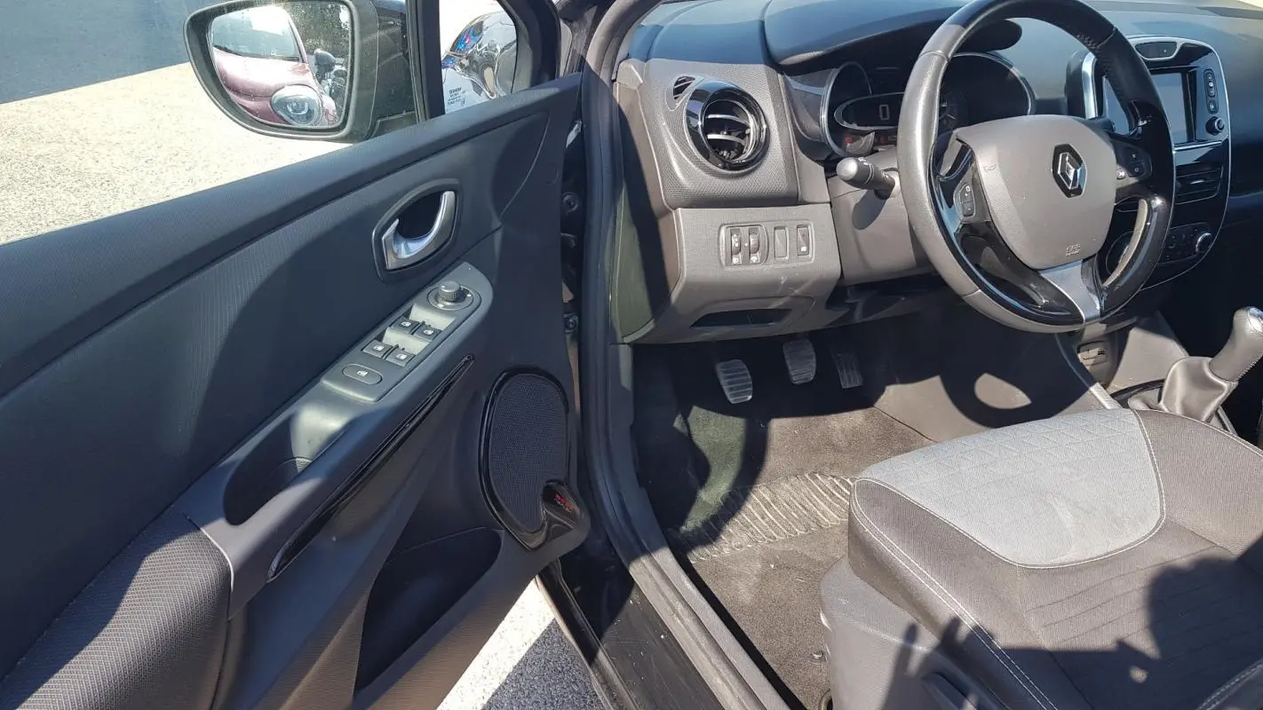 Intérieur côté conducteur d’une Renault Clio IV noire, montrant volant cuir, commandes porte et siège tissu gris.