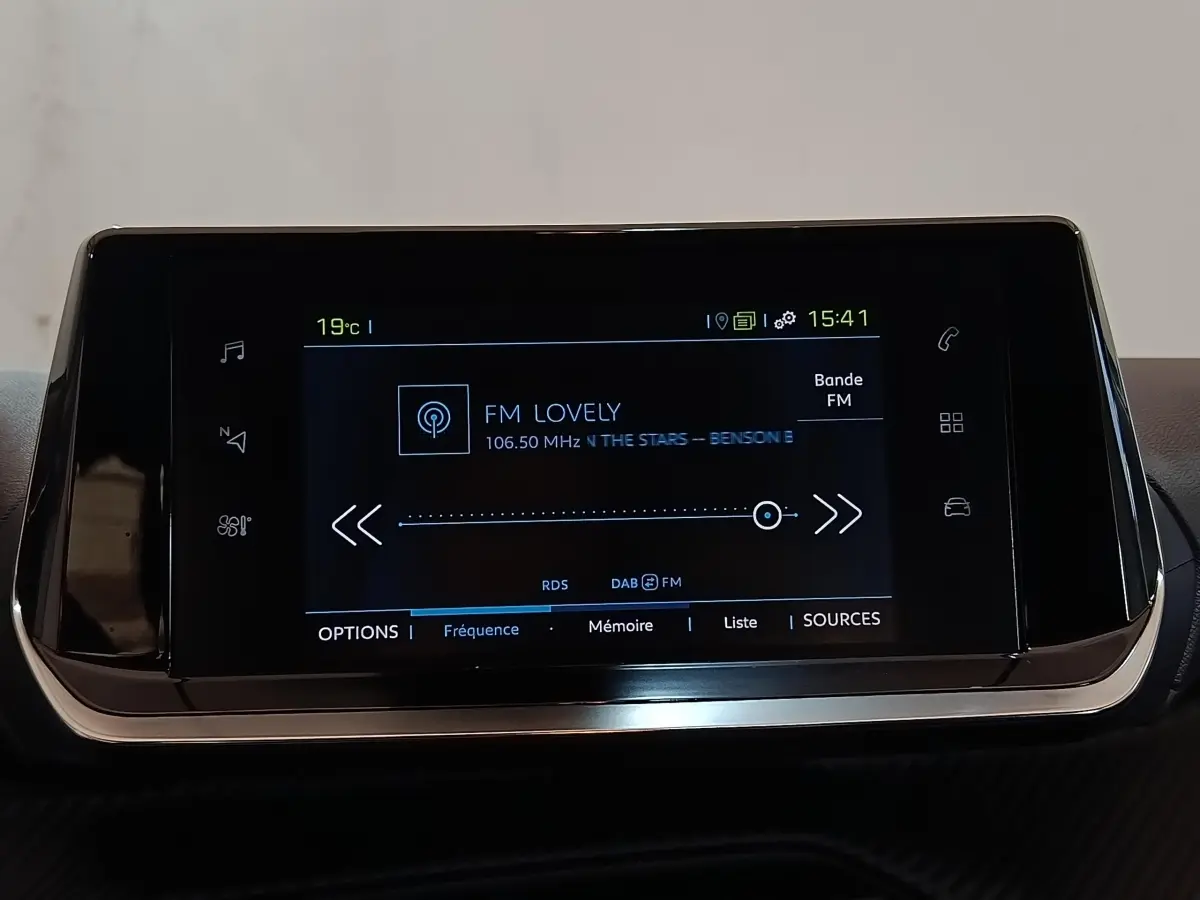 Écran tactile central de 7 pouces affichant la radio FM dans l’habitacle d’une Peugeot 208 blanche électrique.