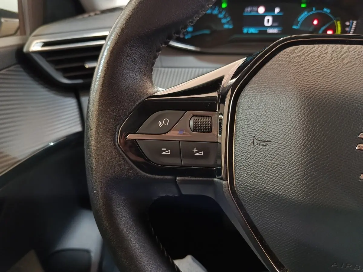 Gros plan sur le volant noir de la Peugeot 208 électrique 2020, avec commandes intégrées et tableau de bord lumineux en arrière-plan.