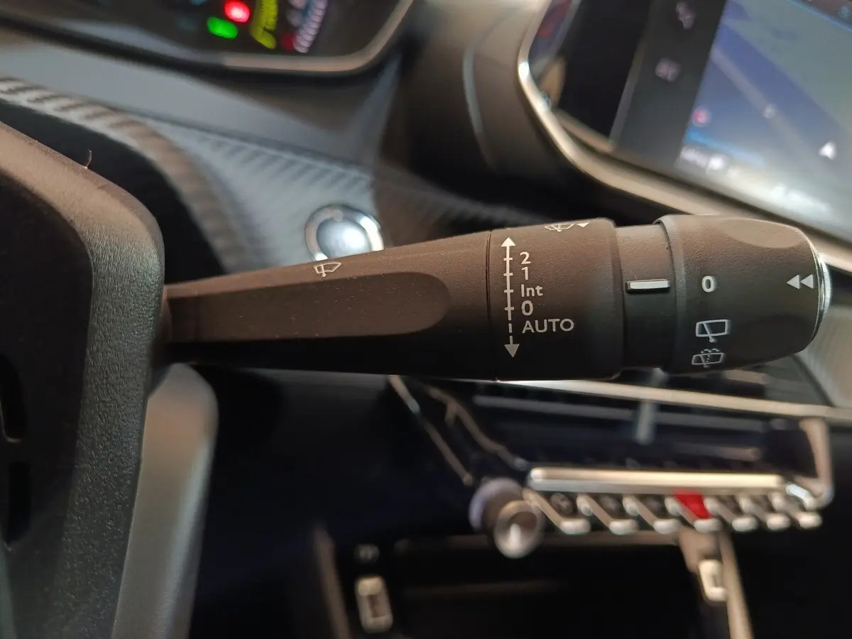 Gros plan sur la commande des essuie-glaces dans l’habitacle noir d’une Peugeot 208 électrique blanche.