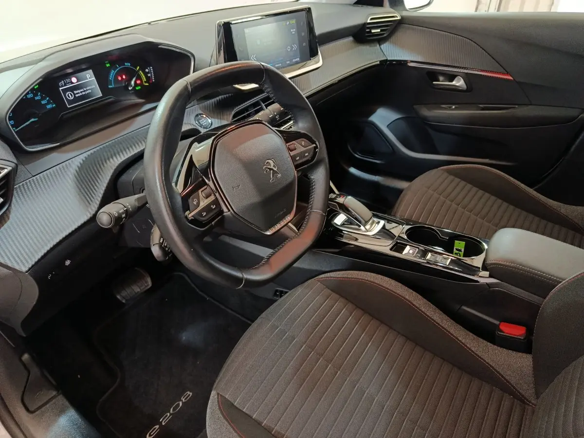 Vue intérieure côté conducteur de la Peugeot 208 électrique, tableau de bord numérique et volant cuir noir.