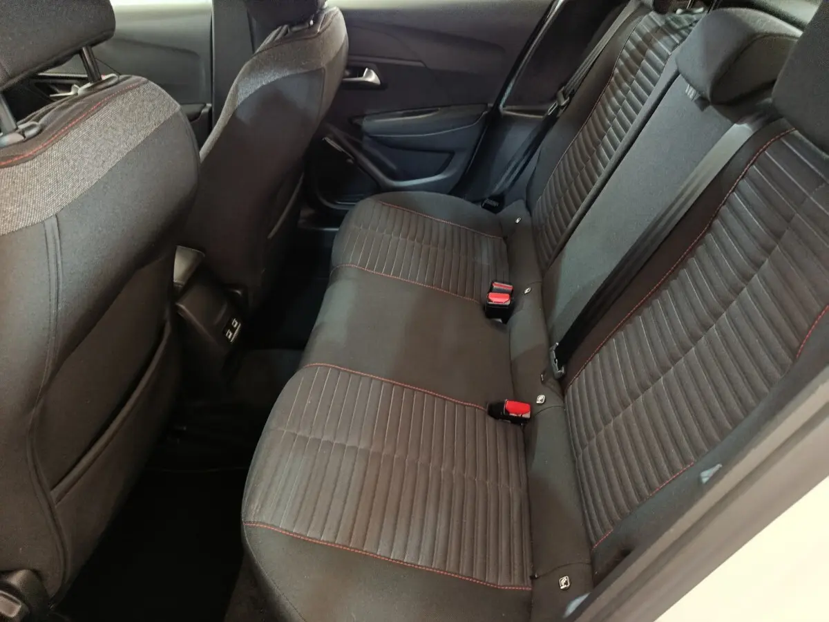 Vue côté droit de la banquette arrière noire avec surpiqûres rouges dans l’habitacle d’une Peugeot 208 blanche électrique.