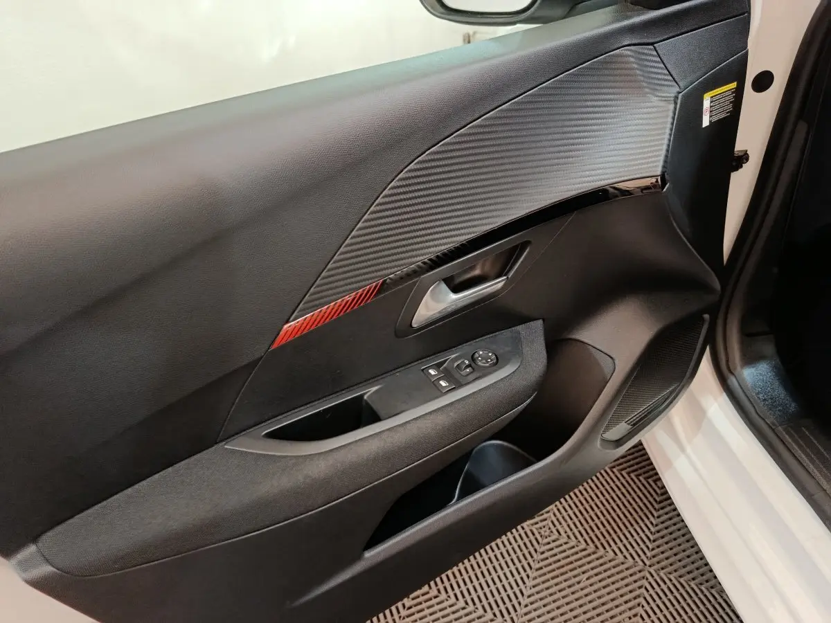 Vue intérieure de la porte avant droite de la Peugeot 208 électrique blanche, avec insert décoratif rouge et commandes électriques.