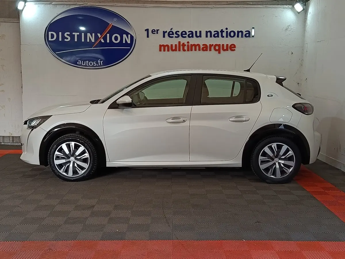 Profil latéral droit d'une Peugeot 208 Electrique Active Business blanche, stationnée en intérieur avec jantes distinctives.