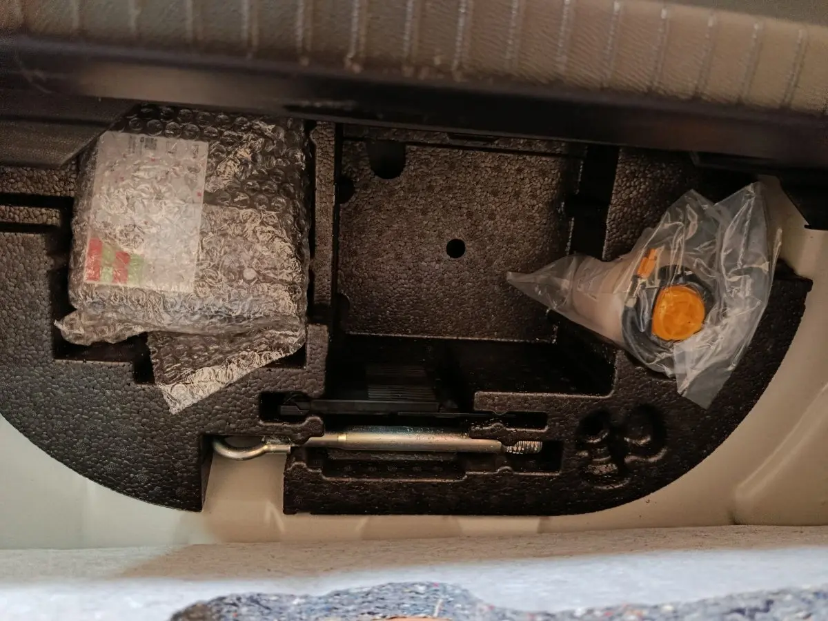 Vue du compartiment sous la banquette arrière d'une Peugeot 208 blanche, montrant le rangement d'outils et accessoires.